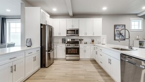 Una cocina moderna con armarios blancos, electrodomésticos de acero inoxidable y un piso de madera con patrón de espiga.