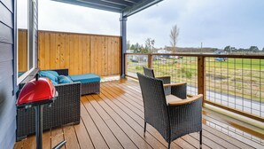 Una terraza techada al aire libre con mobiliario de mimbre, una parrilla y vistas a un campo de césped.