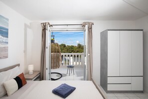 A hotel room with a bed, a nightstand, a lamp, a wardrobe, a balcony with a wicker chair, and a view of trees and sky. - Croatia/Istria🇭🇷🌊🏖️☀️ villa-liznjan a villa 2 apartments (Ližnjan)