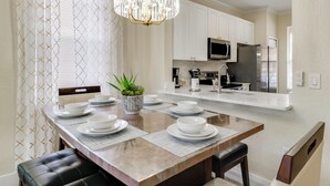 A modern kitchen with white cabinets, a stainless steel refrigerator, and a dining area with a wooden table set for four. - Disney Magic & Resort Fun! Family Gem in Davenport (Davenport)