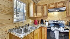 Una cucina con pensili in legno, lavandino in acciaio inox, fornello e finestra con persiane.