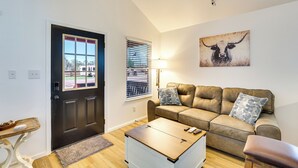 Een woonkamer met een bruine leren bank, een houten salontafel, een zwarte deur, een raam met zonwering en een wandlamp.