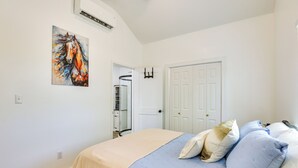 Een slaapkamer met een bed, een deur, een airconditioning en een schilderij aan de muur.