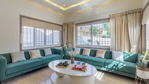 Un salon moderne avec un canapé vert, une table basse en marbre et de grandes fenêtres dotées de rideaux.