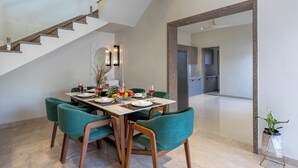 Un coin repas avec une table dressée pour quatre personnes, des chaises à revêtement vert, un escalier en bois et un grand miroir accroché au mur.