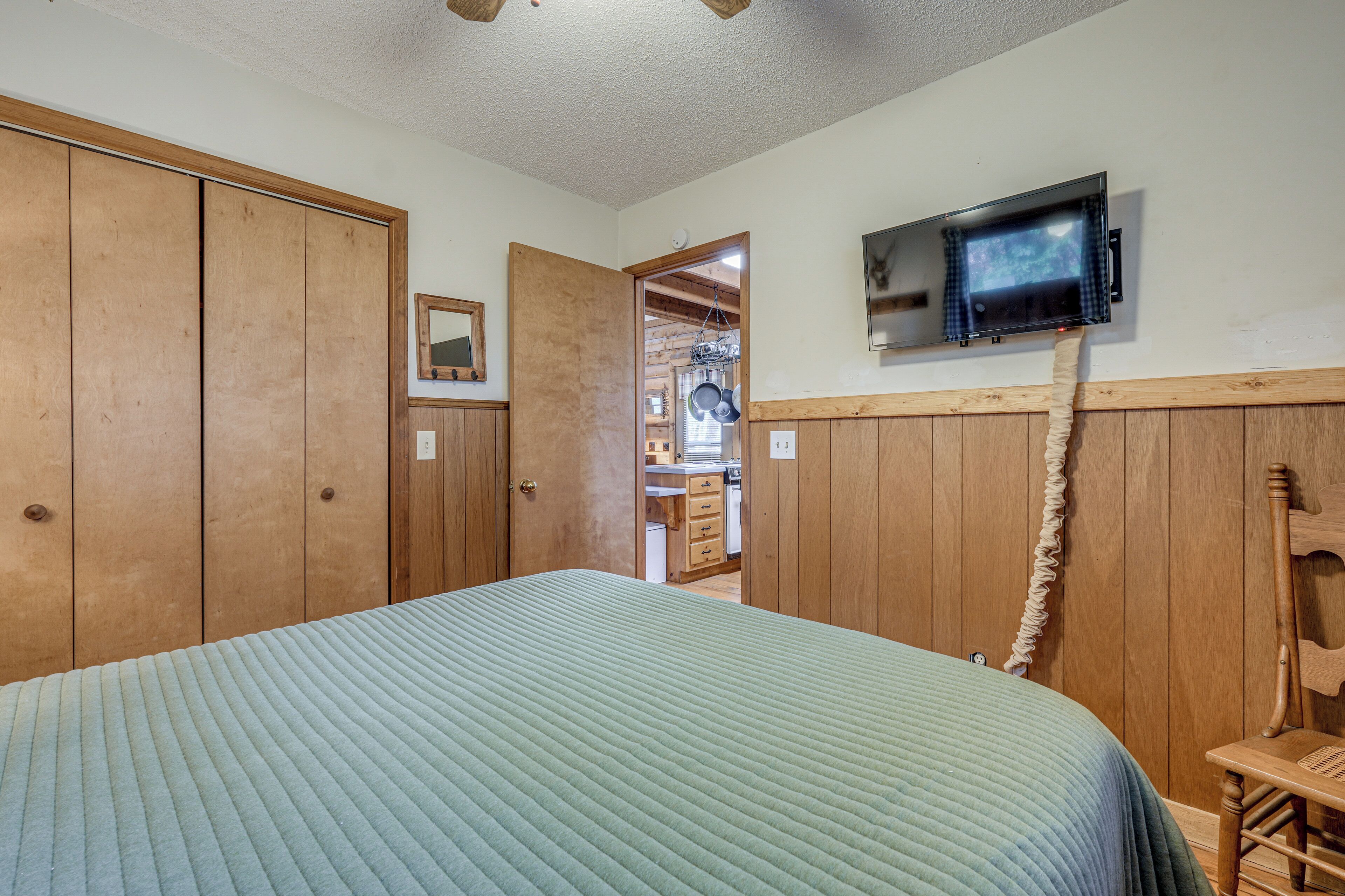 Une chambre à coucher comprenant un lit, une armoire en bois, un téléviseur fixé au mur et une chaise en bois.