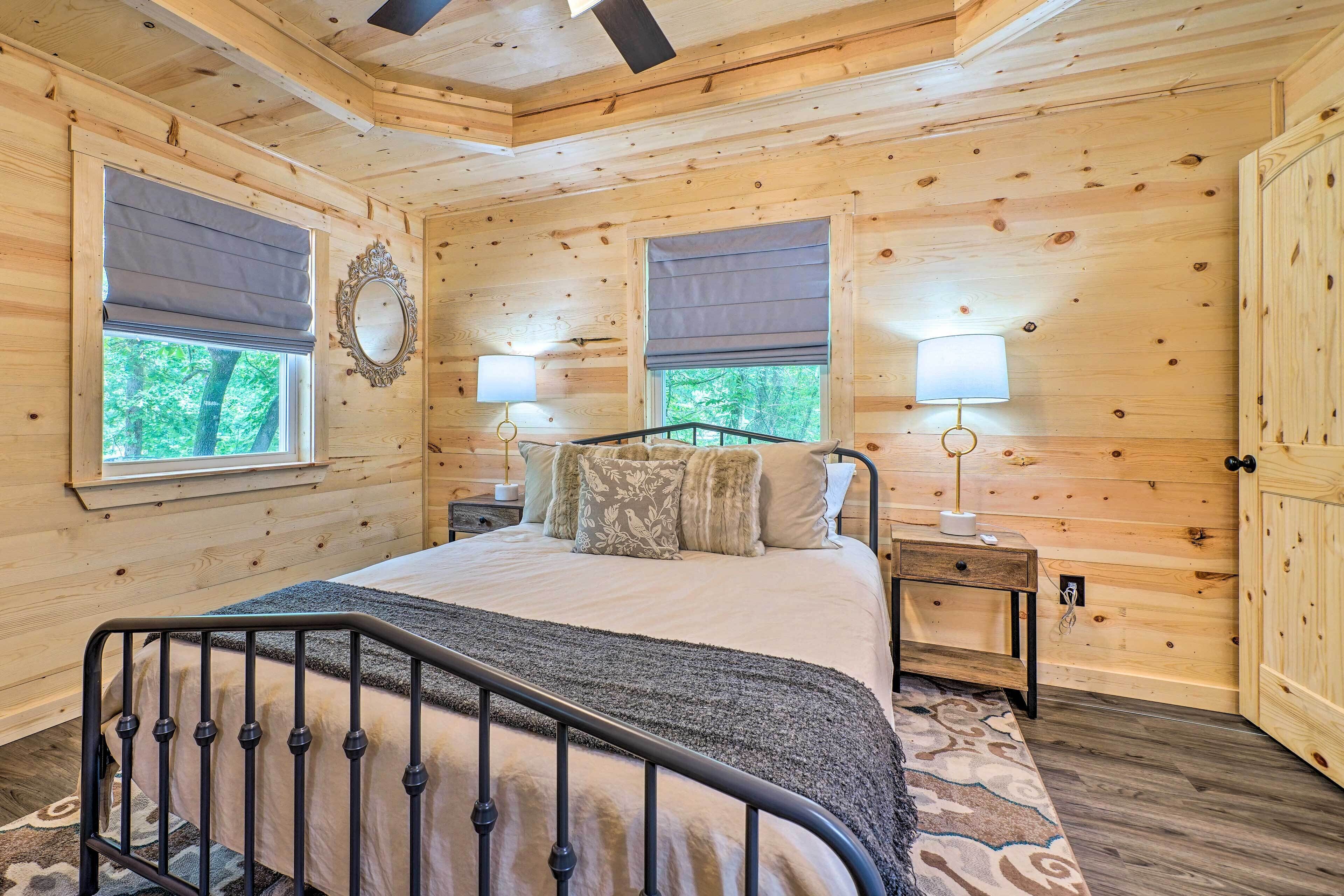 Ein Schlafzimmer einer Holzhütte mit einem Bett, zwei Nachttischen und einem Fenster mit Blick auf Bäume.