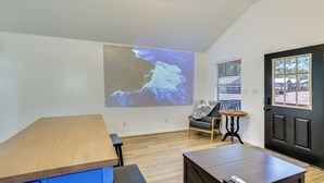 A modern interior with a wooden table, a projection screen displaying a landscape, a black door, and a window with blinds. - Fish, Boat & Explore! Tiny Cabin Near Sabine River (Joaquin)