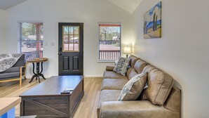 A living room with a sofa, coffee table, and two windows with blinds. - Fish, Boat & Explore! Tiny Cabin Near Sabine River (Joaquin)