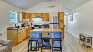 A modern kitchen with wooden cabinets, a stainless steel refrigerator, and a central island with stools. - Fish, Boat & Explore! Tiny Cabin Near Sabine River (Joaquin)