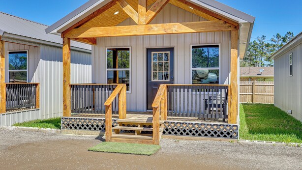 A single-story building with a wooden porch, a fenced yard, and a clear blue sky. - Fish, Boat & Explore! Tiny Cabin Near Sabine River (Joaquin)
