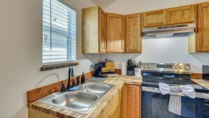 A kitchen with wooden cabinets, a stainless steel sink, a stove, and a window with blinds. - Fish, Boat & Explore! Tiny Cabin Near Sabine River (Joaquin)