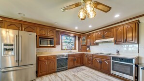Una cocina con armarios de madera, electrodomésticos de acero inoxidable, lavavajillas y ventilador de techo.