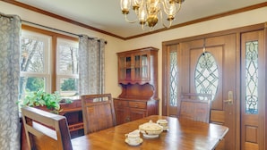 Comedor con mesa de madera, sillas, una lámpara de araña y una puerta de vidrio emplomado.