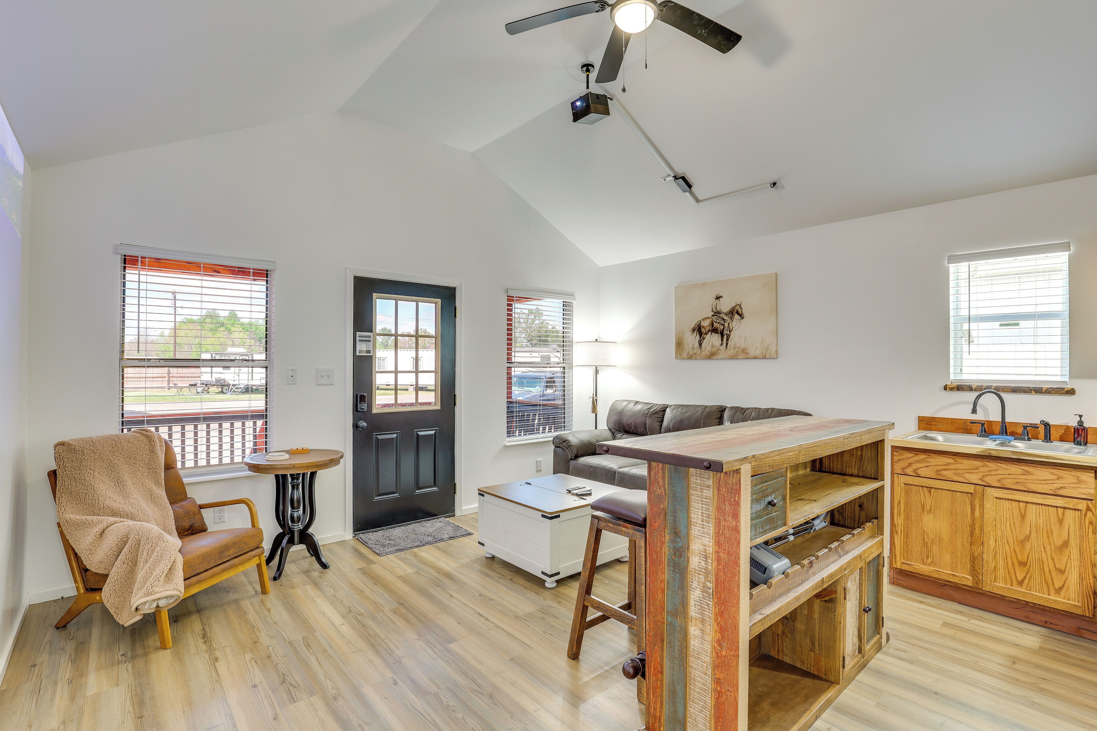 Un espacio habitable amplio con un sofá, una mesa de centro, una silla, una cocina con armarios de madera y un ventilador de techo.