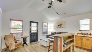 A spacious living area with a sofa, a coffee table, a chair, a kitchen with wooden cabinets, and a ceiling fan.