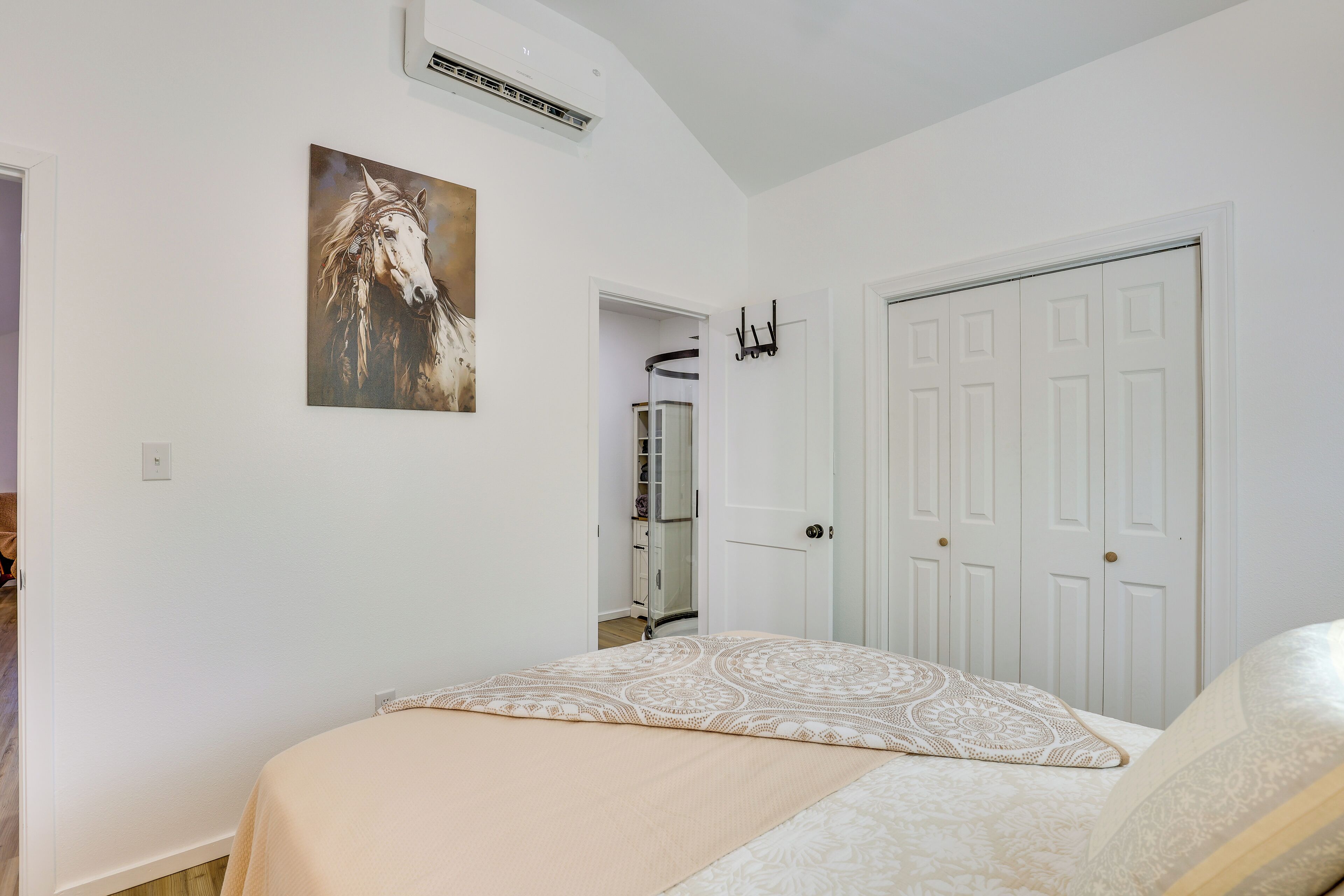 Un dormitorio con cama, una puerta, perchero y un cuadro en la pared.