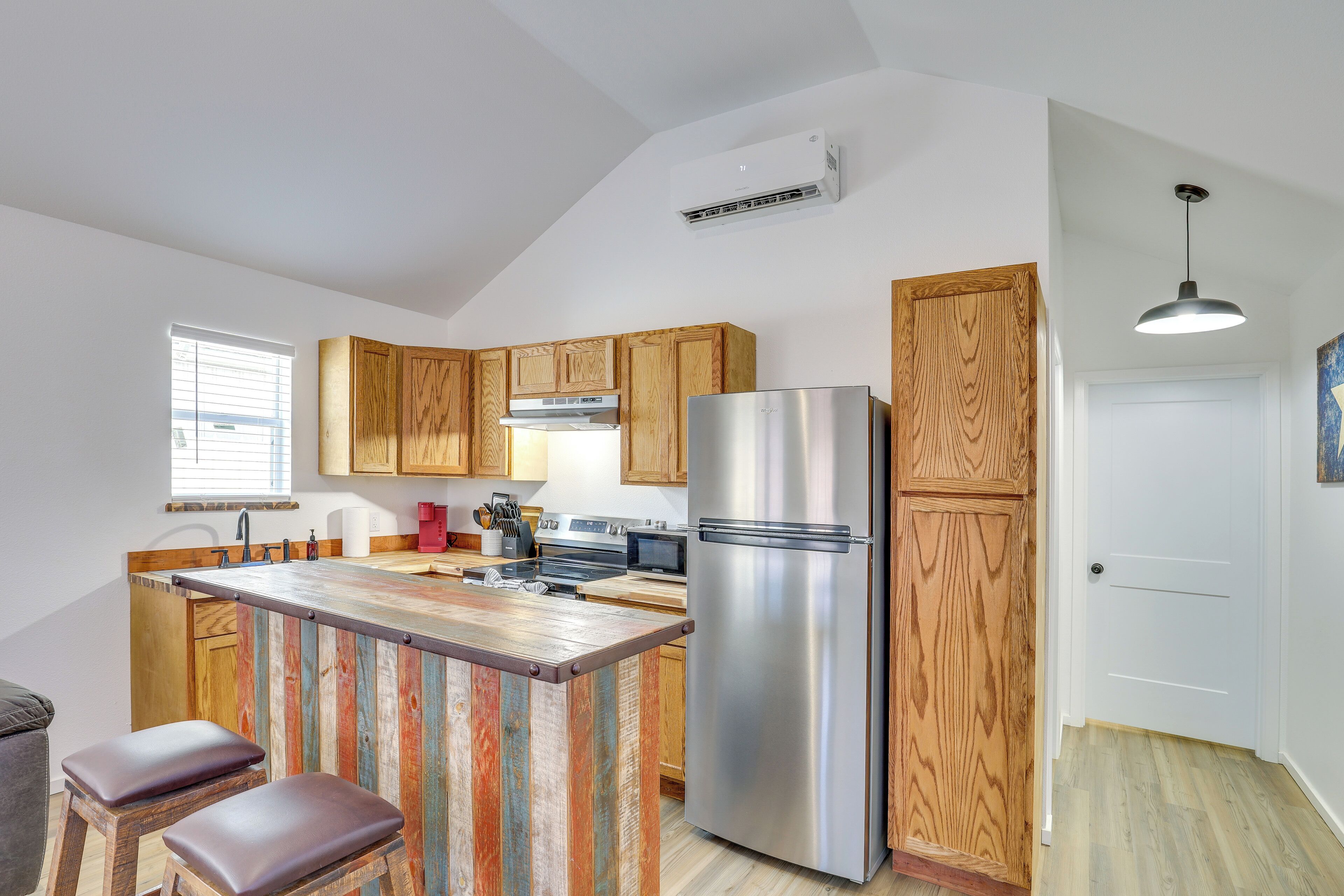 Una cocina con armarios de madera, un refrigerador de acero inoxidable y una zona de bar con taburetes.