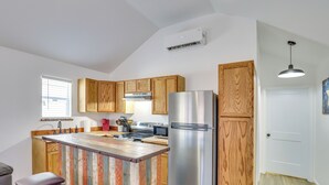 A kitchen with wooden cabinets, a stainless steel refrigerator, and a bar area with stools.