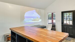 A room with a wooden table, a projection of a beach scene, a door, and a window with a view of the outside. - 3 Mi to Sabine River! Modern Cabin Retreat (Joaquin)