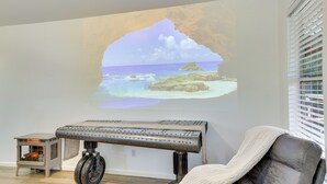 A room with a projection of a beach scene, a keyboard, a chair with a blanket, and a small heater. - 3 Mi to Sabine River! Modern Cabin Retreat (Joaquin)