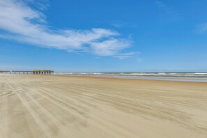 A wide sandy beach with a pier extending into the water. - Sleek, Oceanfront Unit in Daytona Beach Shores! (Daytona Beach Shores)