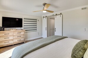 A bedroom with a bed, a ceiling fan, a TV, a dresser, and a sliding door. - Sleek, Oceanfront Unit in Daytona Beach Shores! (Daytona Beach Shores)