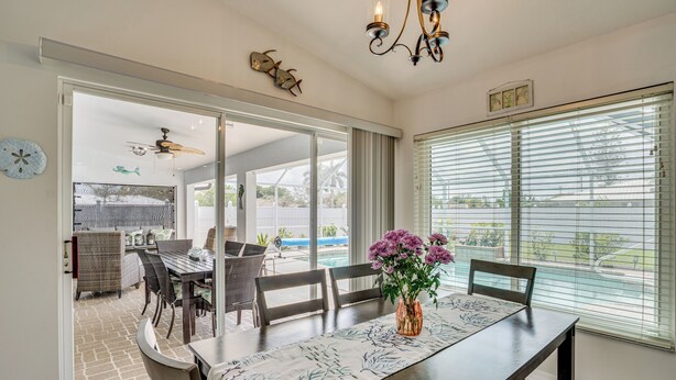 A dining area with a table, chairs, a vase with flowers, and a view through large windows. - Cape Coral Family Home w/ Heated Pool (Cape Coral)