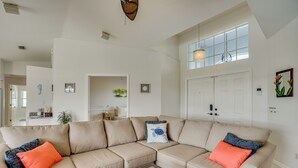 A spacious living room with a large beige sectional sofa, a glass coffee table, and a high ceiling with a unique light fixture. - Cape Coral Family Home w/ Heated Pool (Cape Coral)
