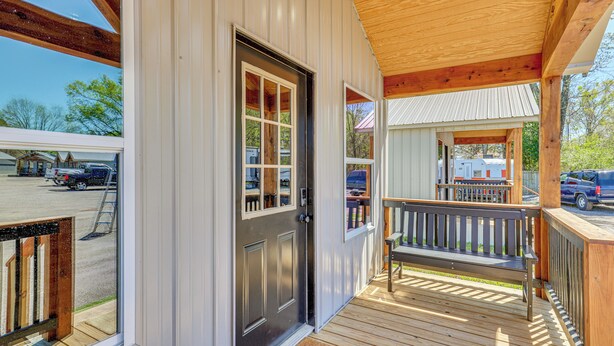 A wooden porch with a bench, a door with glass panels, and a view of a parking lot. - Fish, Explore & Unwind: Couple's Cabin in Joaquin (Joaquin)