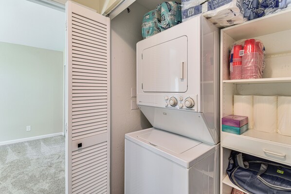 A laundry room with a washer and dryer, storage shelves with cleaning supplies, and a door with louvered panels. - Swim & Golf! 'Jackson Mill Cottage' in Groveland (Groveland)