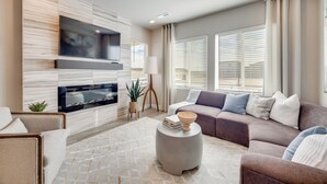 Un salon moderne avec un téléviseur à écran plat, un canapé d’angle, une table basse ronde et une cheminée.