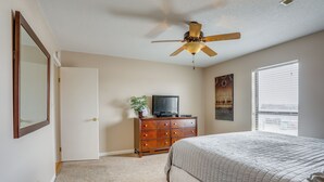 Ein Schlafzimmer mit Bett, Kommode, Deckenventilator, Fernseher und Fenster.