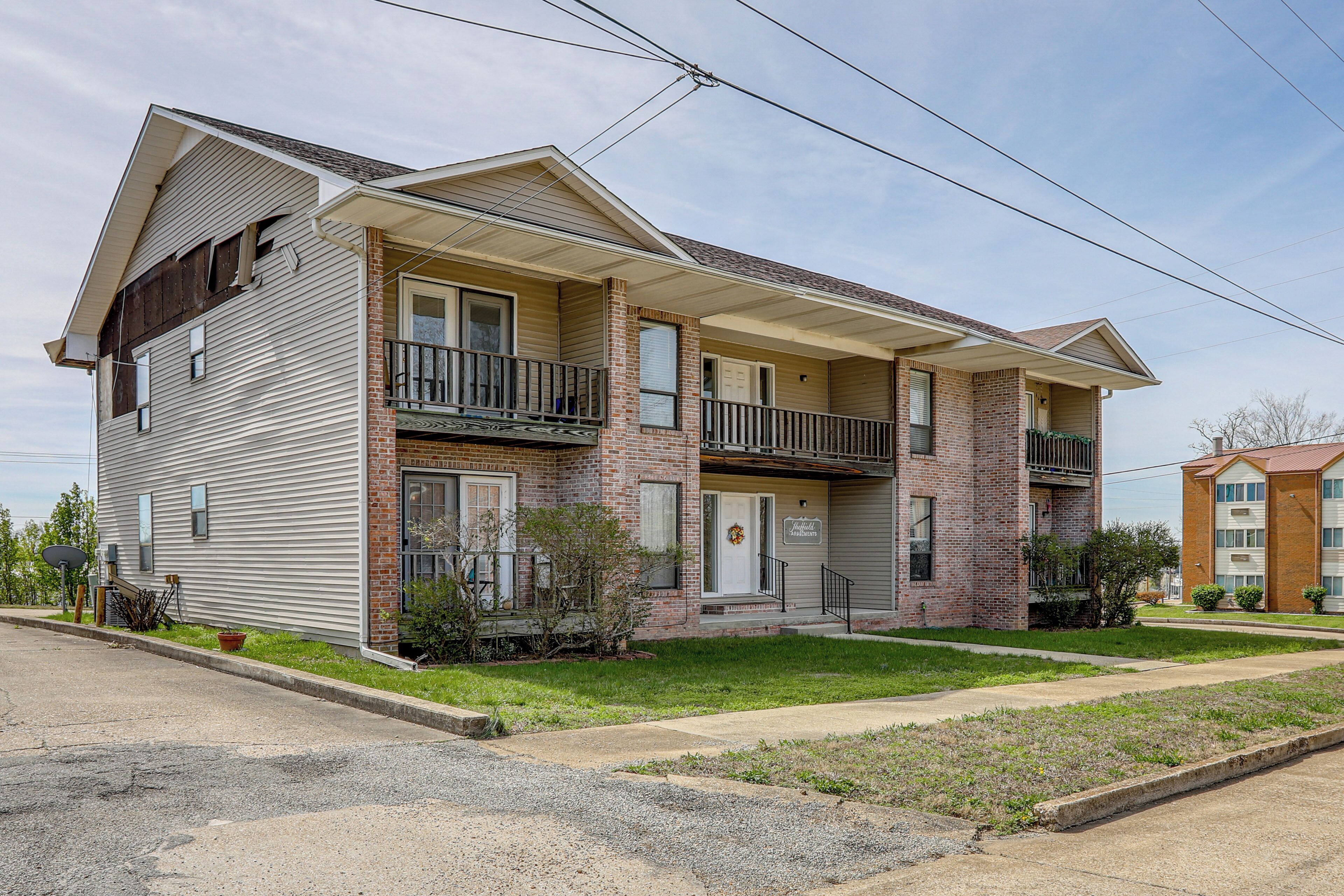 A two-story building with a brick facade, a balcony on the second floor, and a garage door on the ground floor.
