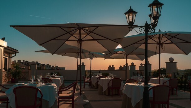Un espace extérieur aménagé pour les repas, avec des tables, des chaises, des parasols et des lampadaires.
