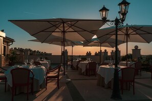 Ein Außenbereich zum Essen mit Tischen, Stühlen, Sonnenschirmen und Laternen.