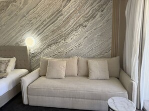 Una habitación moderna con pared con diseño de mármol, un sofá, una cama y una pequeña mesa redonda.