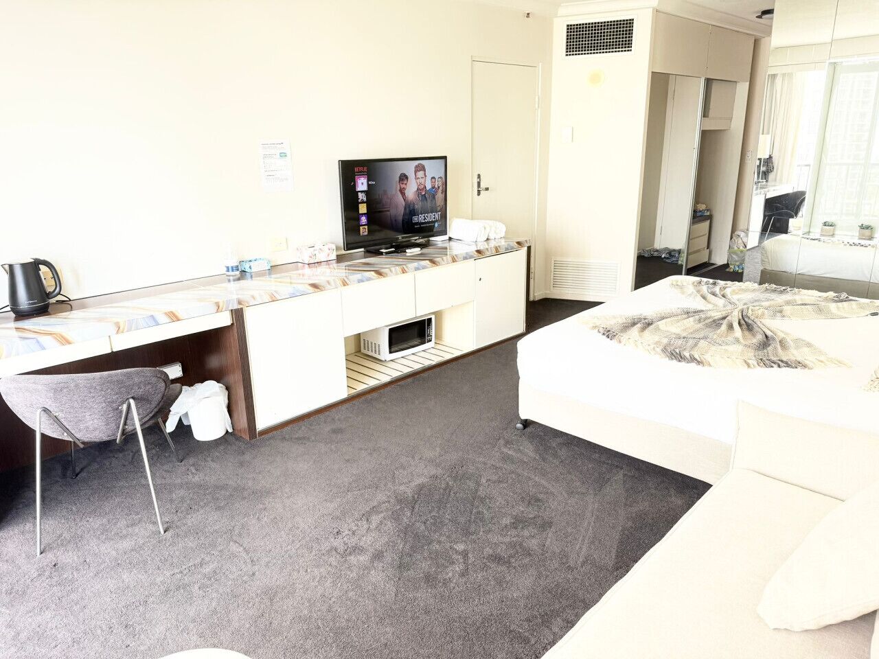 Et hotelværelse med en seng, et skrivebord med computer, et fjernsyn og en mikroovn.