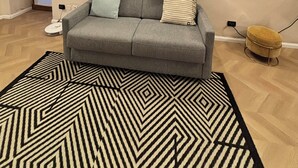 Un salon moderne avec un canapé gris, un tapis à motifs et trois œuvres d’art encadrées accrochées au mur.