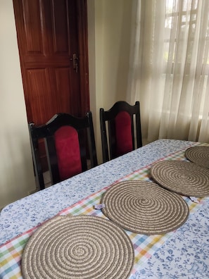 Una mesa de comedor con mantel floral, sillas de madera y caminos de mesa tejidos.