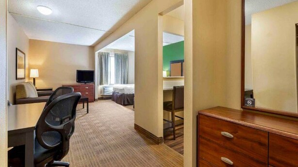 Ein Hotelzimmer mit Bett, Schreibtisch, Stuhl, Kommode und Fernseher.