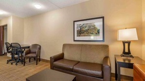 Ein Hotelzimmer mit einem braunen Ledersofa, einem kleinen Tisch mit Lampe, einem gerahmten Bild an der Wand und einem Schreibtisch mit zwei Stühlen.