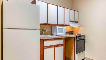A compact kitchen with a refrigerator, microwave, stove, and wooden cabinets.