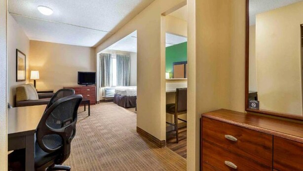 A hotel room with a bed, desk, chair, TV, dresser, and a mirror. - 1 Queen Bed | Suite, Non-Smoking, Kitchen (Florence)