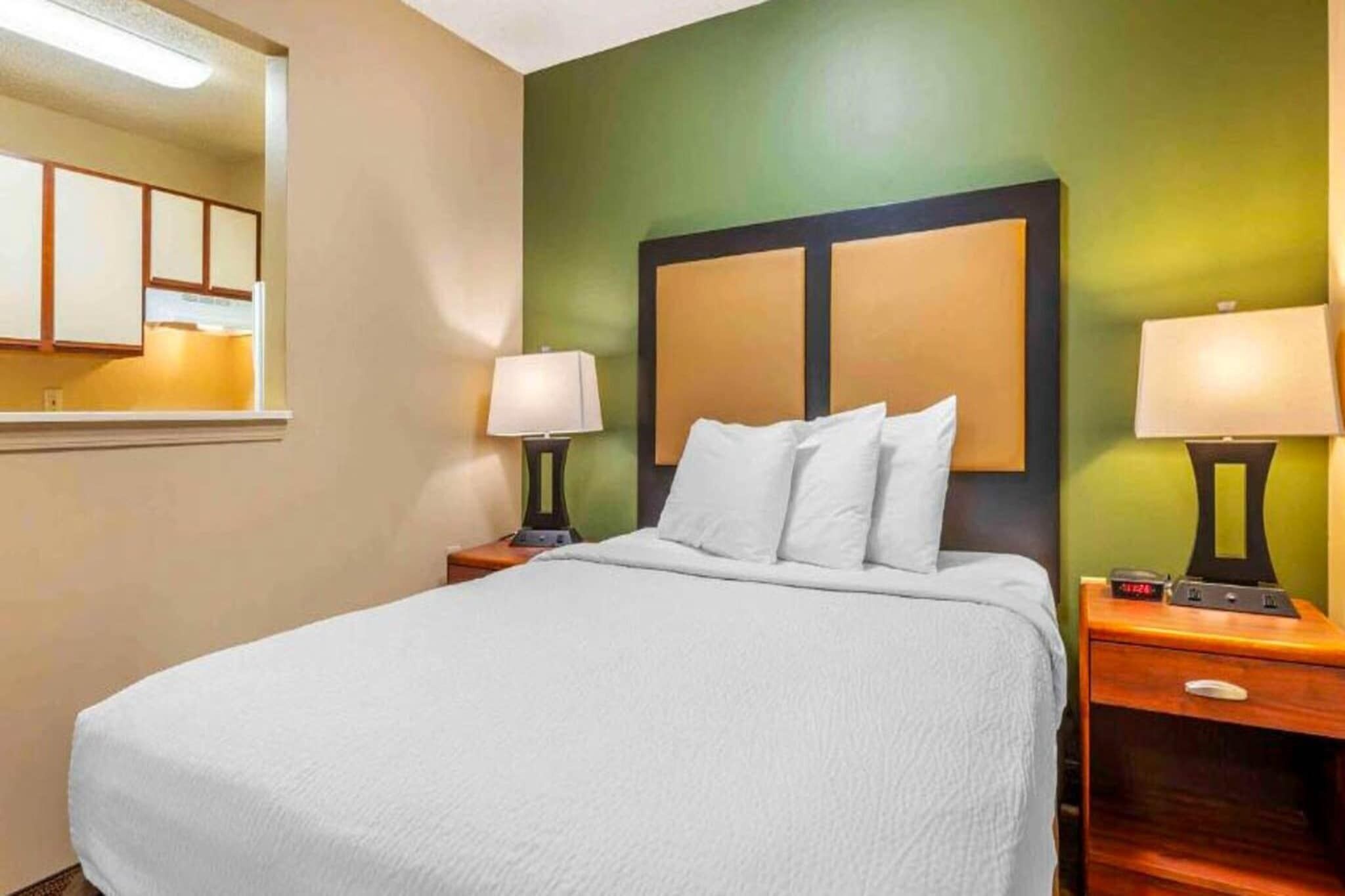 A hotel room with a bed, two bedside tables with lamps, a mirror, and a green accent wall.