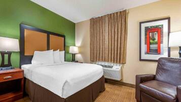 A hotel room with a bed, a desk, a chair, a window with curtains, and a framed picture on the wall.
