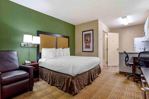 Una habitación de hotel con cama, escritorio, silla, lámpara y un cuadro en la pared.