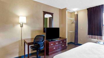 A hotel room with a bed, a desk with a chair, a television, a dresser, a mirror, and a shower.