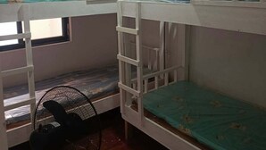 Asuntolan huone, jossa on kerrossängyt, työpöytä, tuoli ja lattiatuuletin.