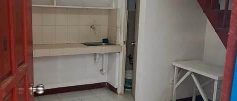 A room with a tiled floor, a white sink, a small table, and a staircase.